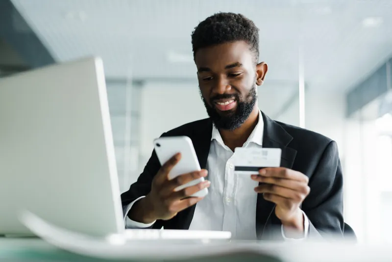 Un homme en costume sourit en réglant un achat par carte sur son téléphone.