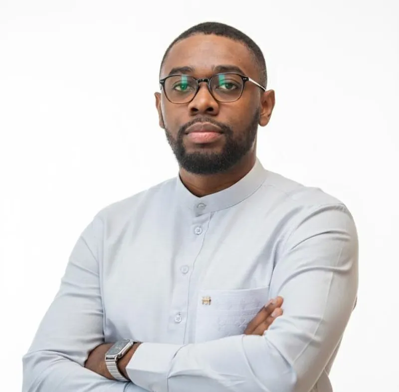 Portrait de Joel Nguema, en chemise gris clair à col officier, bras croisés.