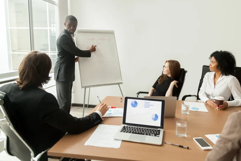 Un consultant anime une séance au tableau devant une équipe réunie.
