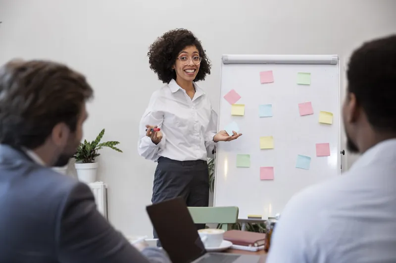 Une consultante présente à son équipe un tableau couvert de notes adhésives.