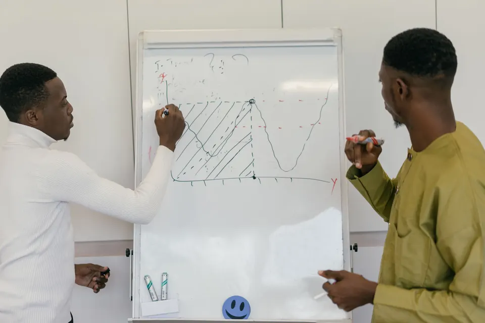 Deux collègues analysent une courbe sur un tableau blanc.